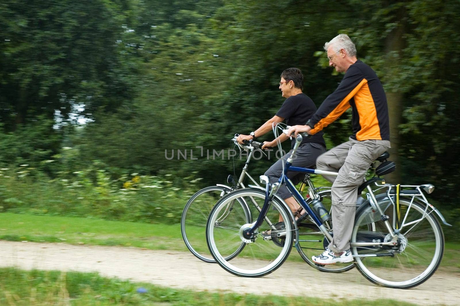 Seniors biking on a sandy path with motion in the picture. Focus is on the woman.