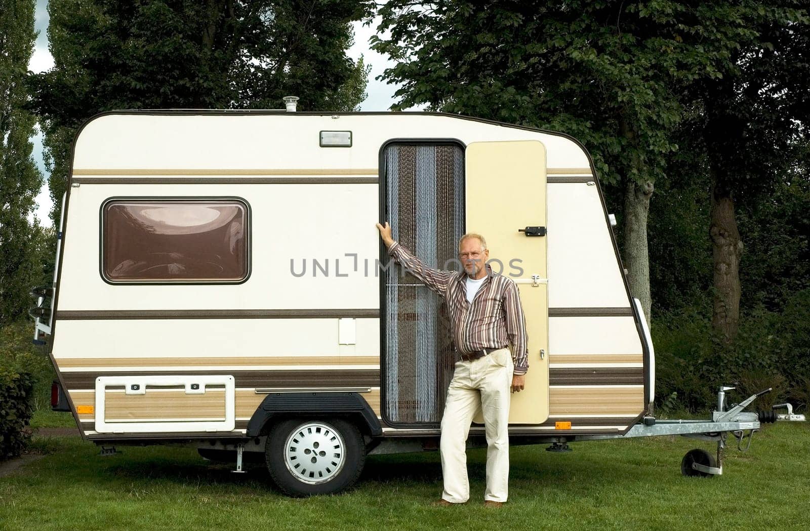 Senior man standing in front of his caravan