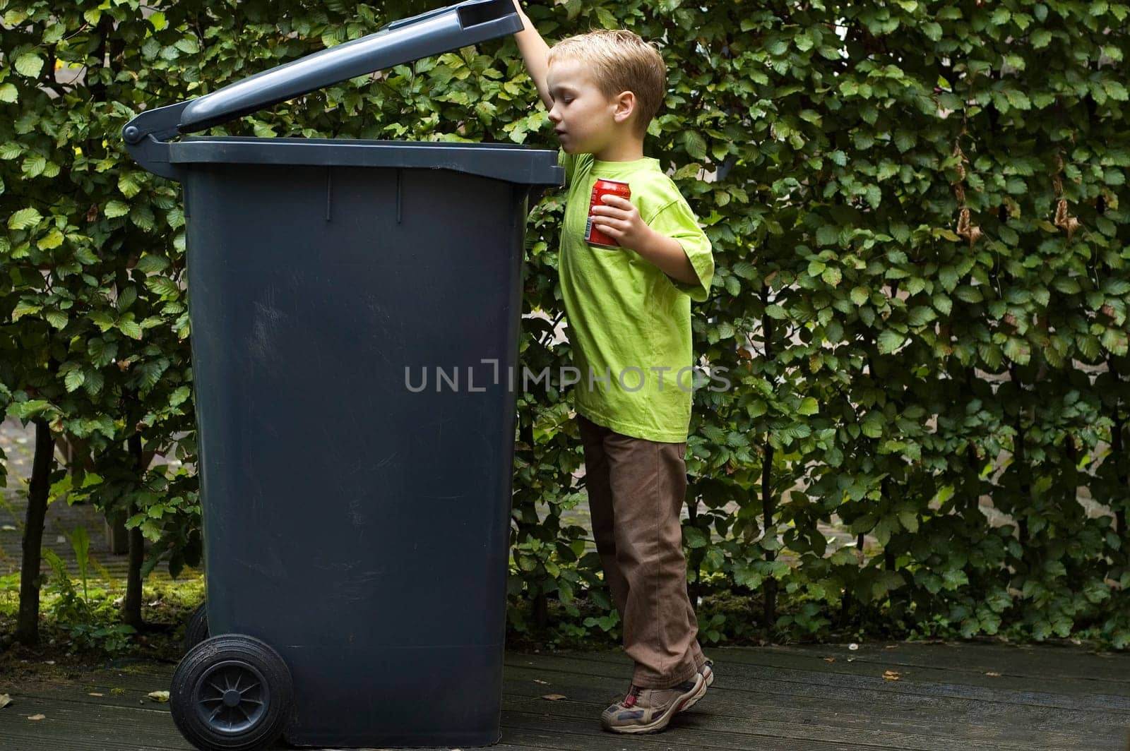 Boy wanting to throw a can in the container, he is learning to be aware that recycling is important.