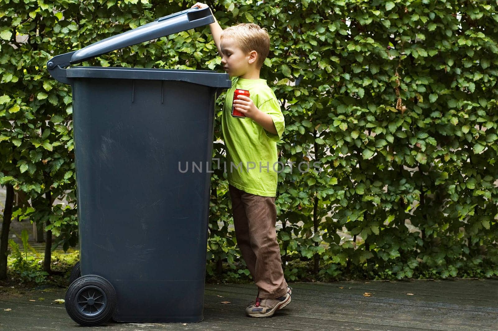 Boy wanting to throw a can in the container, he is learning to be aware that recycling is important.