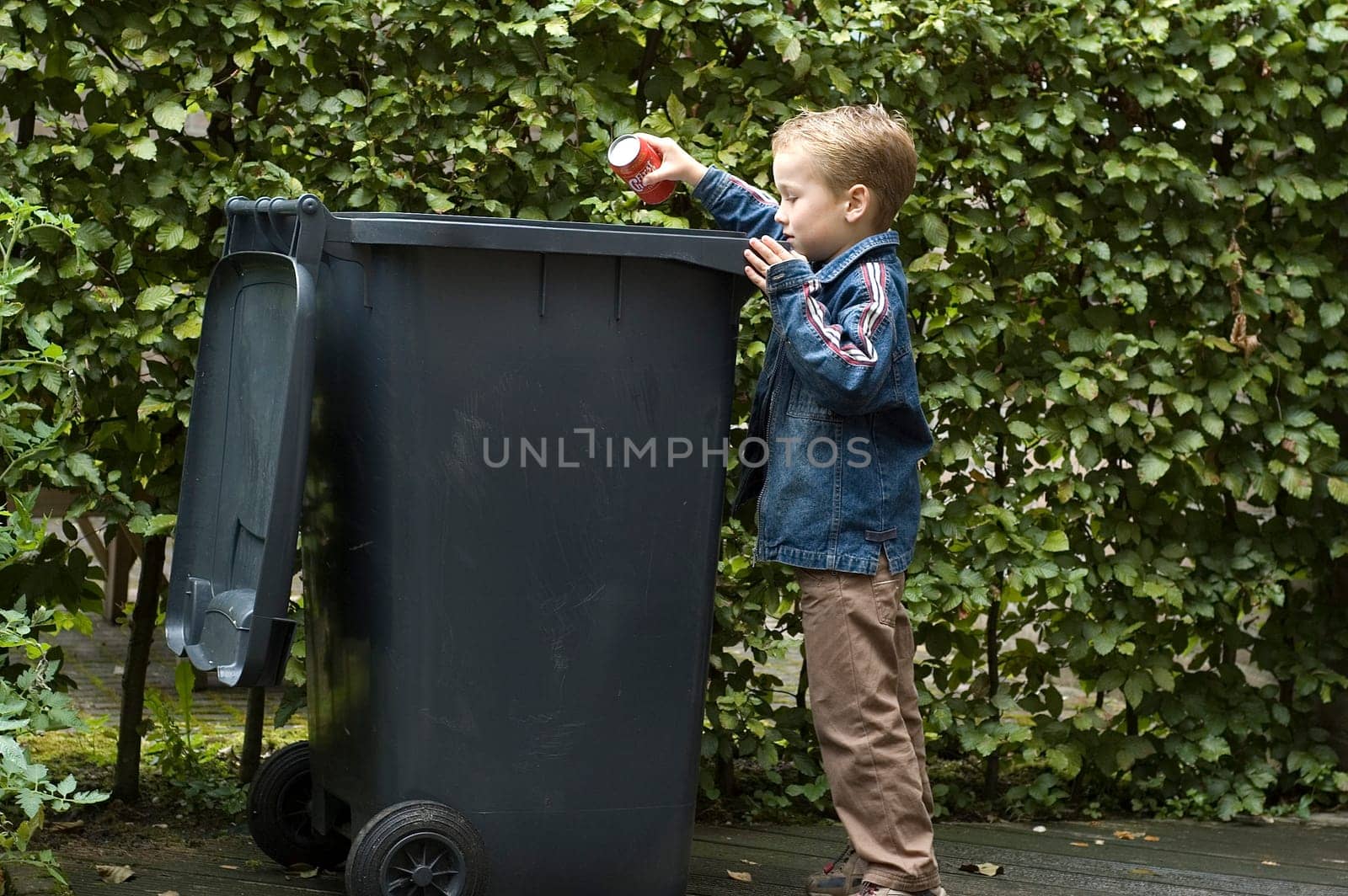 Boy wanting to throw a can in the container, he is learning to be aware that recycling is important.