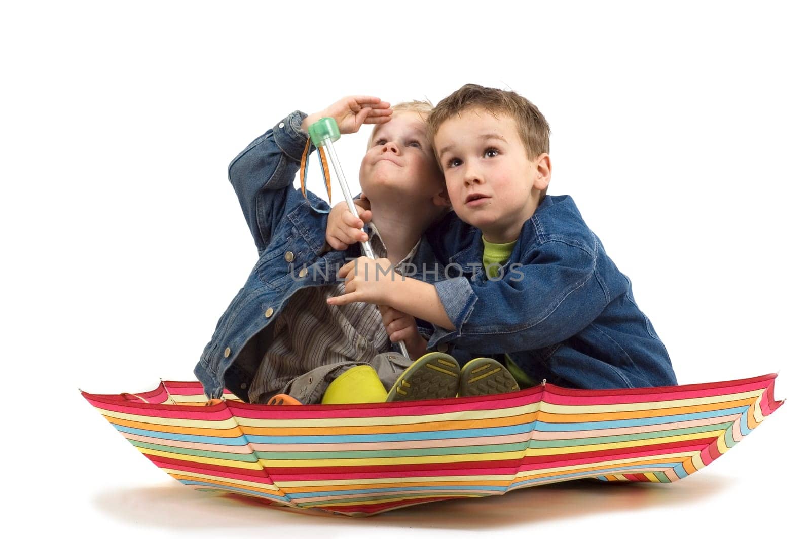 Two boys sitting in an umbrella, like it's a boat. They're watching if the storm is coming.