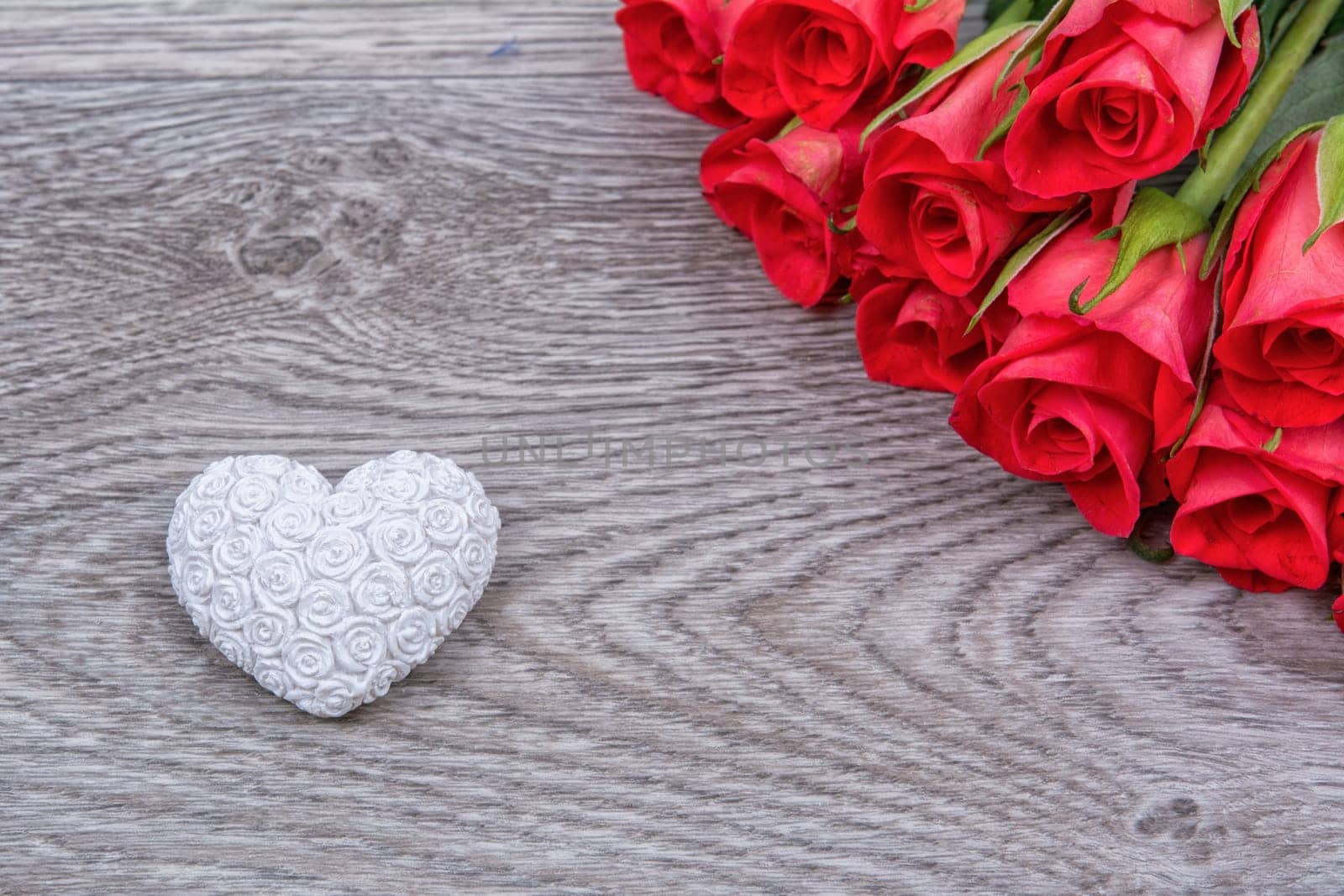 White heart and red roses on a wooden background