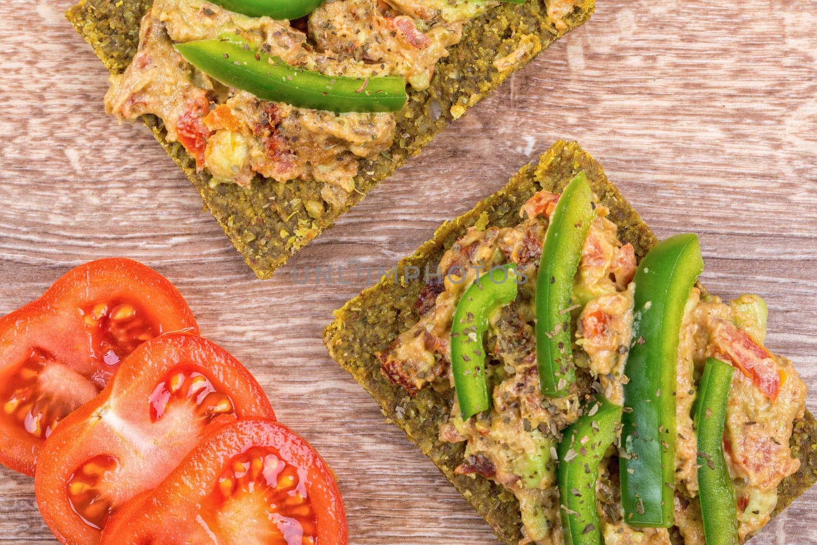 Raw bread with a spread decorated with green pepper and tomatoes
