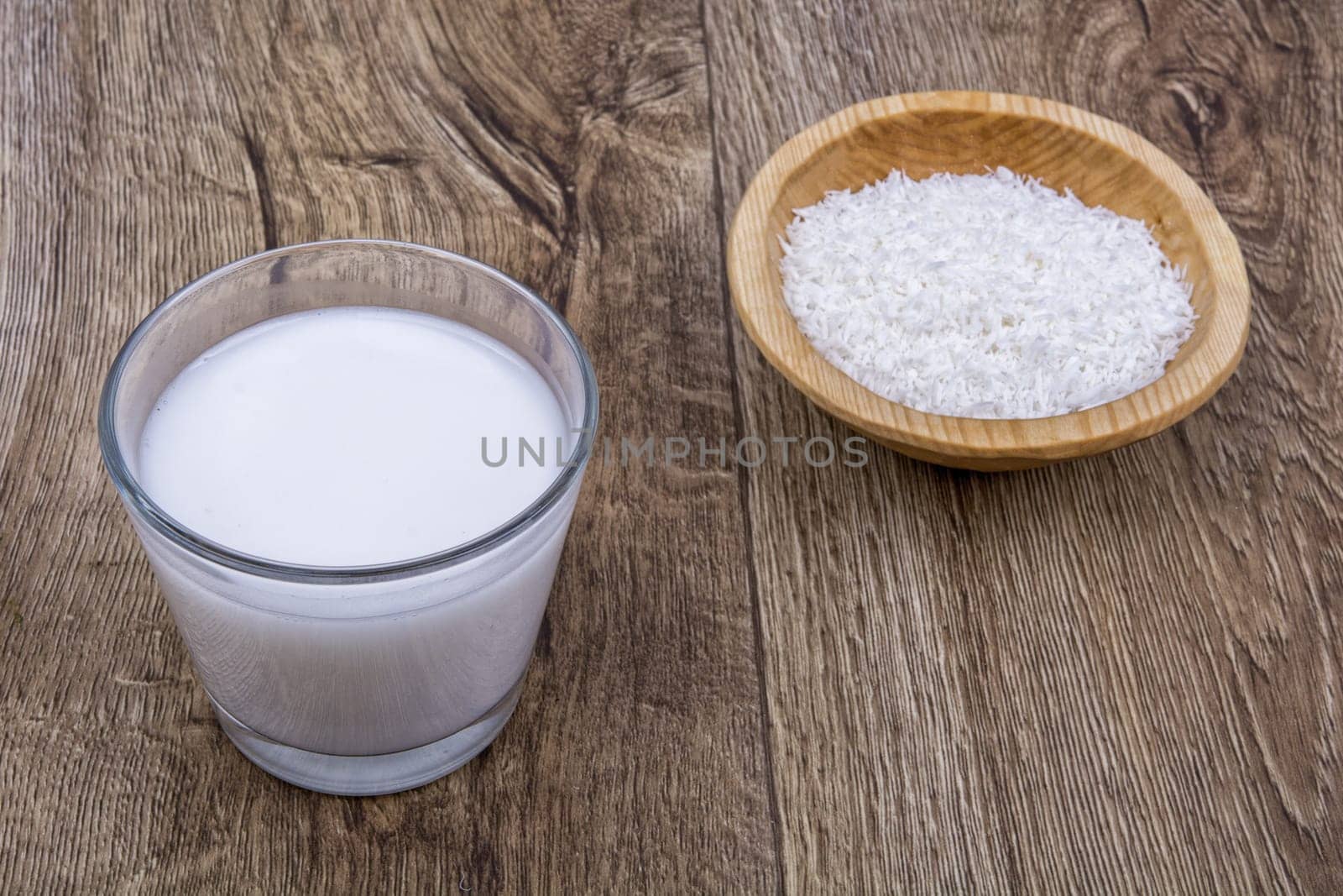 Coconut milk and the dish with grated coconut on a wooden background