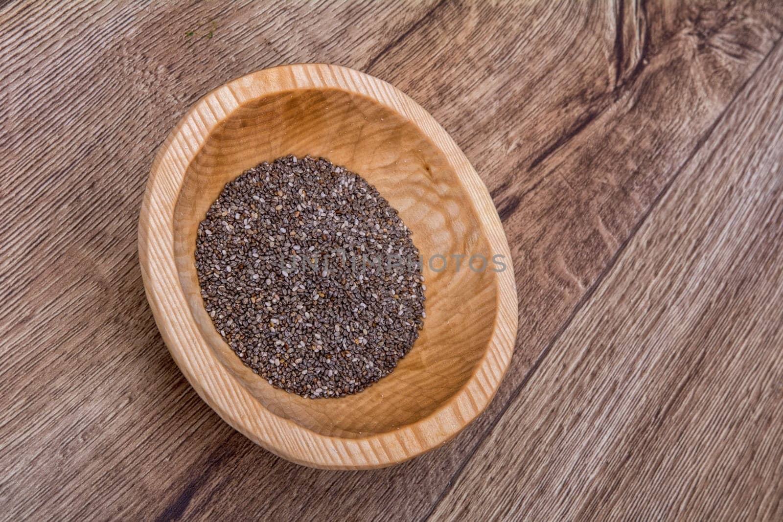 Chia seeds in a wooden bowl on a brown wooden background