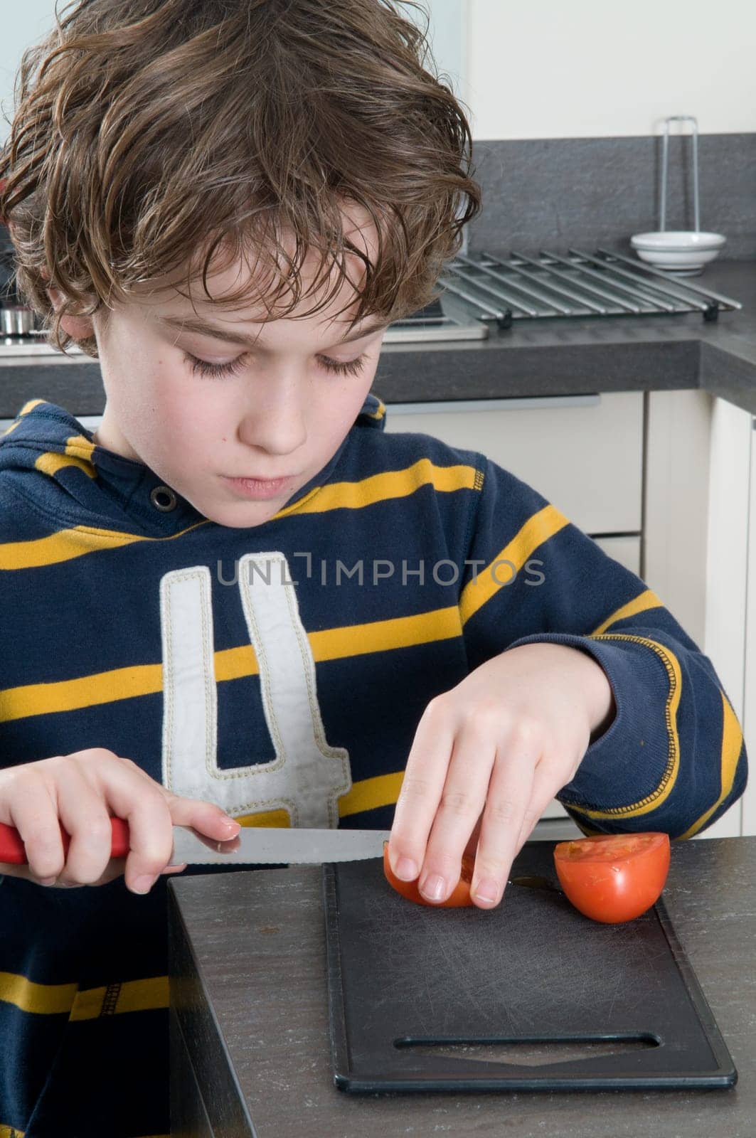 Boy cutting a tomato, getting ready to cook.