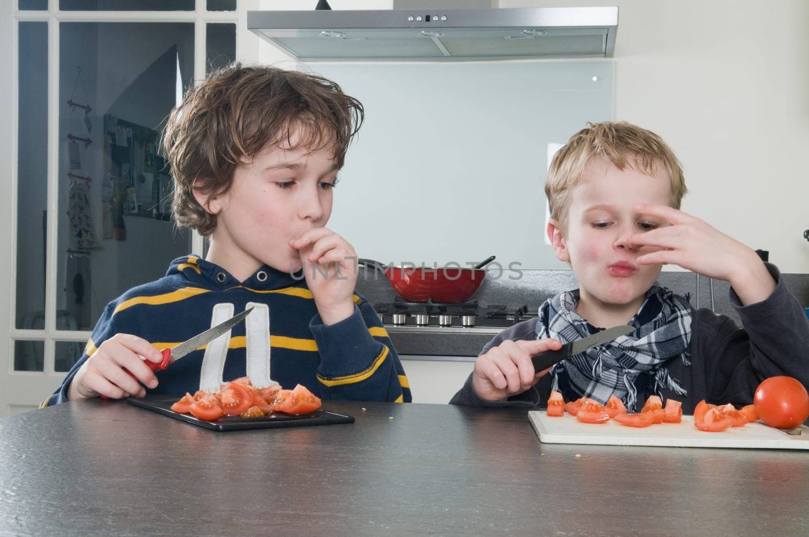 Two boys tasting the just cutted tomatos, used for cooking.