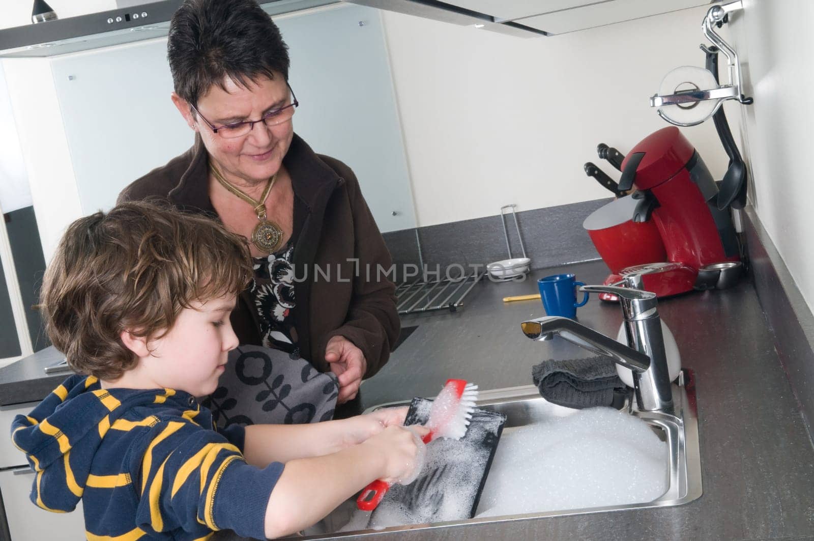 Young boy doing the dishes while grandma is helping.