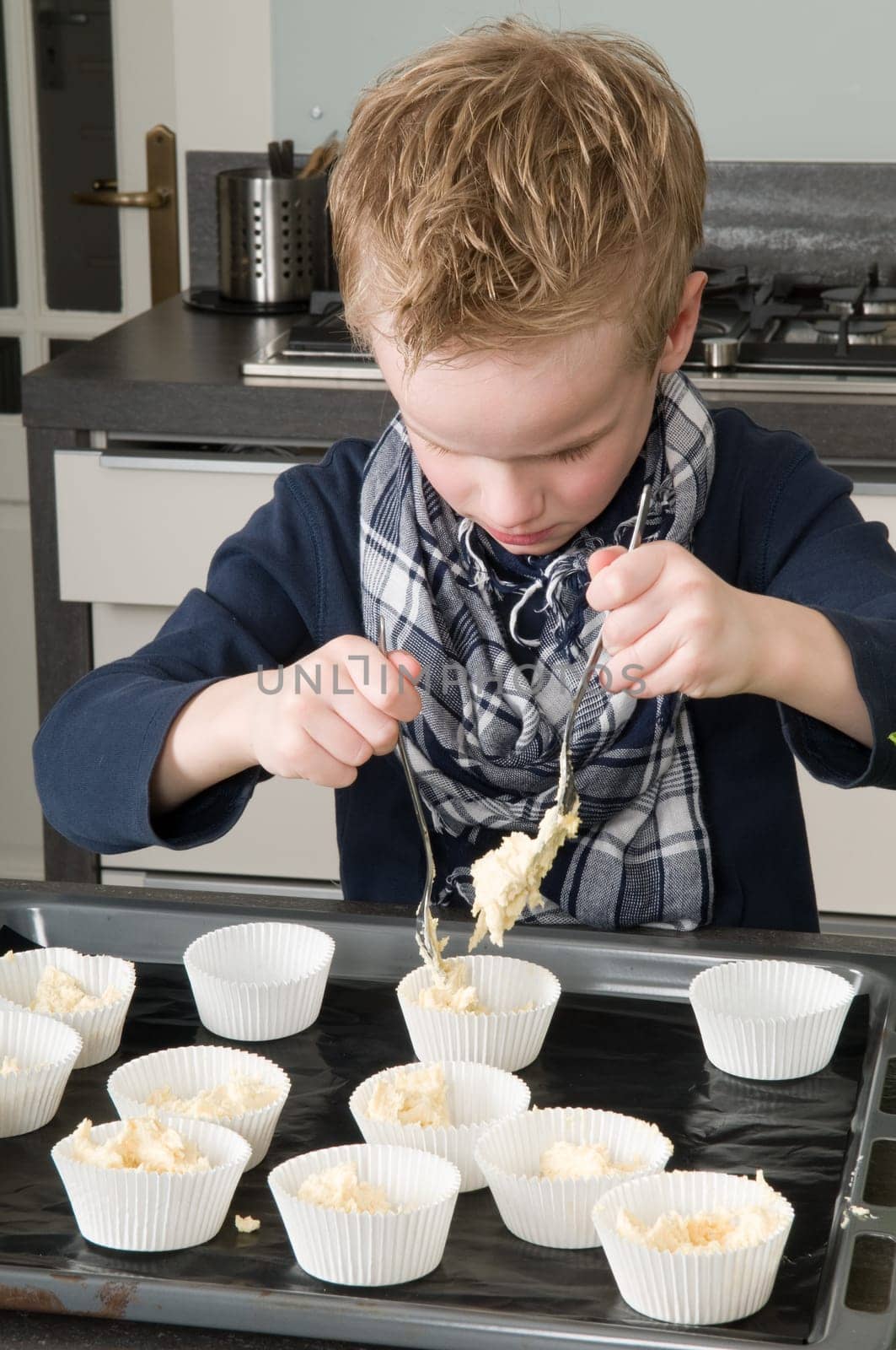 Kid filling the cakecups with the dough, for baking cakes.