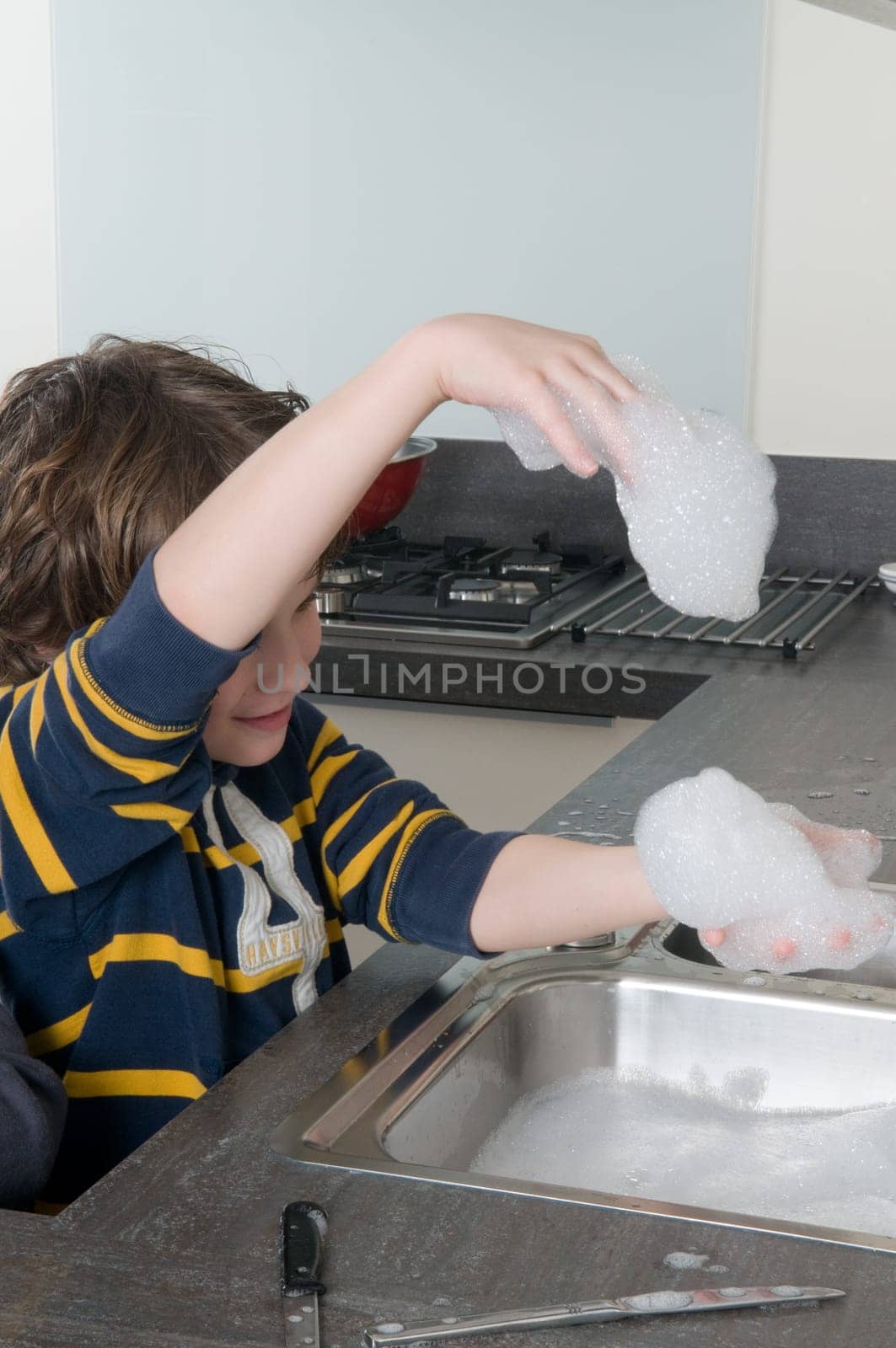 Boy having fun with soap while doing the dishes