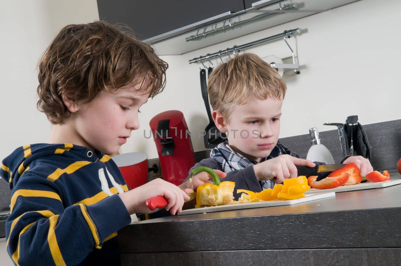 Two boys cutting some red and yellow peppers, used for cooking.