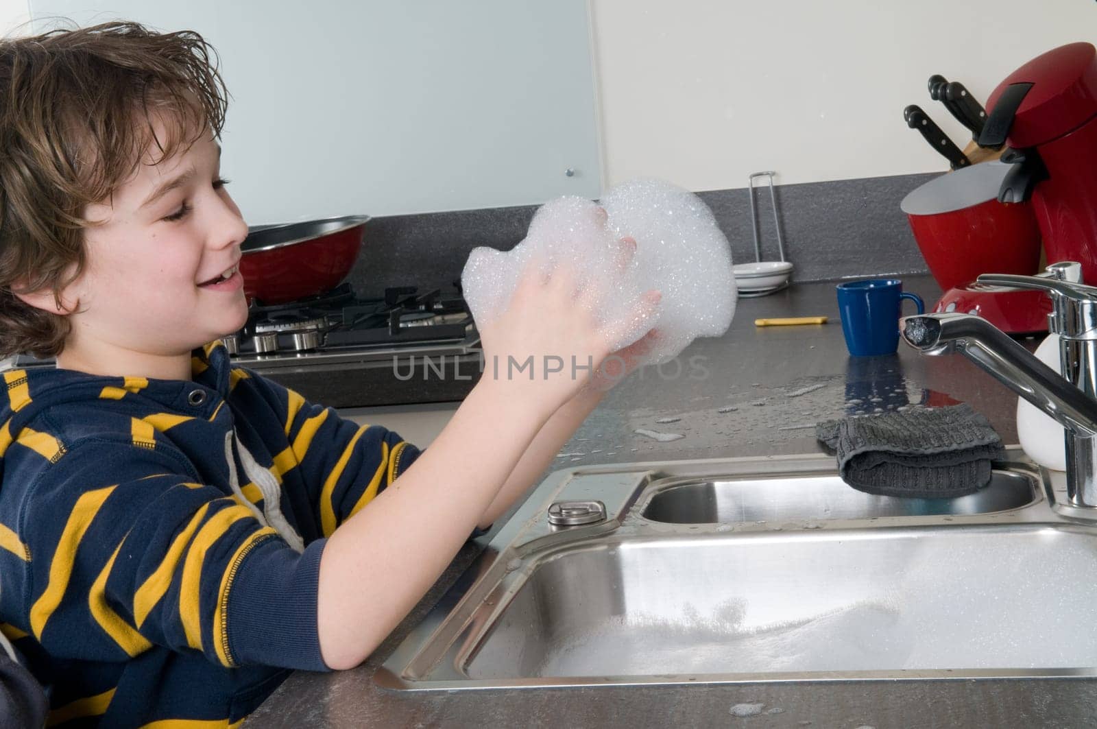 Boy having fun with soap while doing the dishes