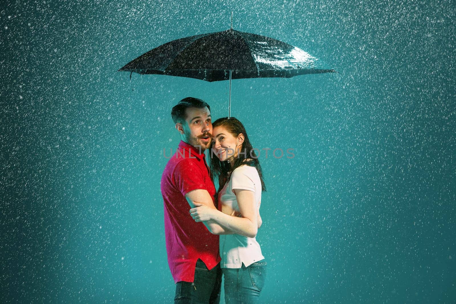 The loving couple in the rain with umbrella on a turquoise background