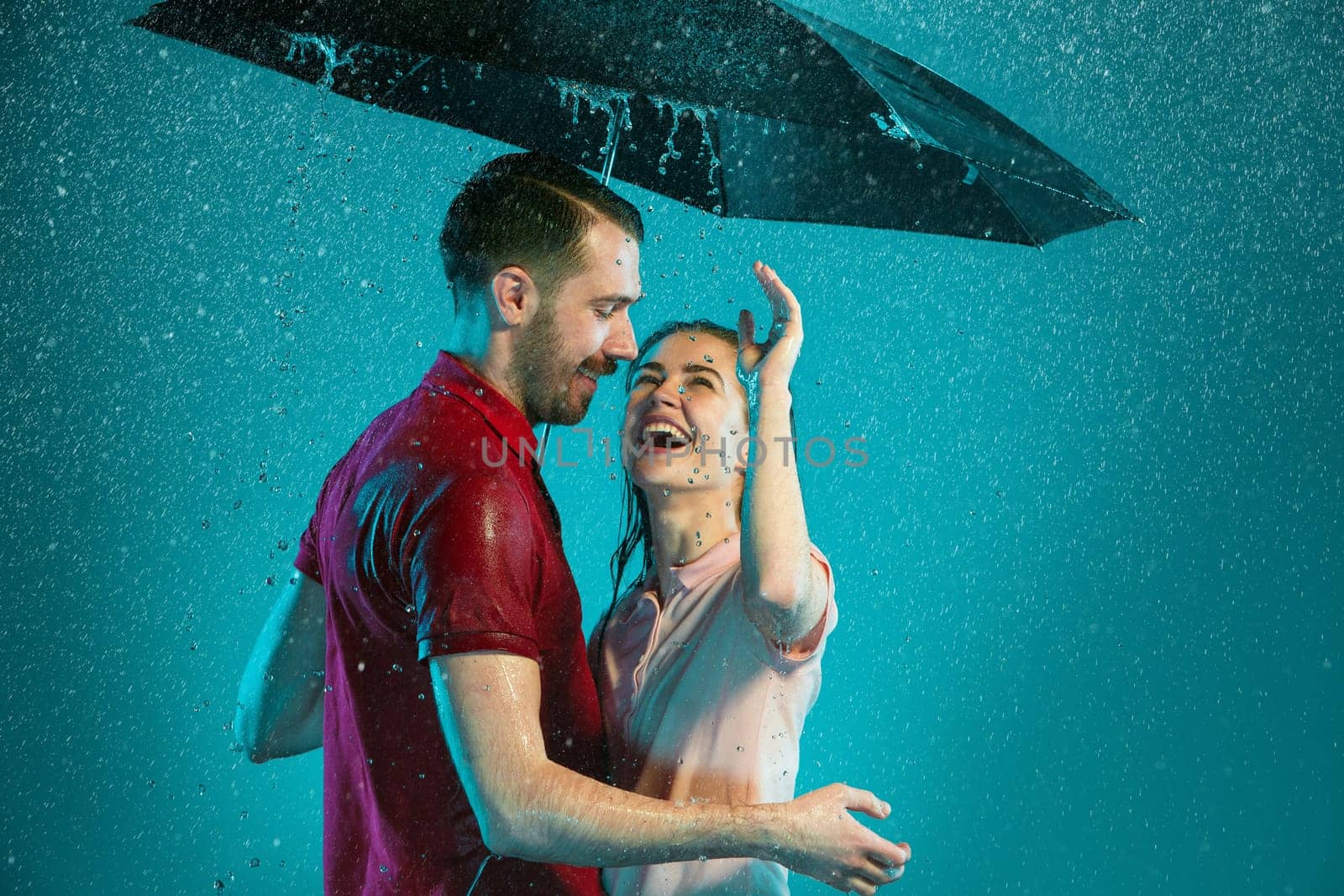 The loving couple in the rain with umbrella on a turquoise background