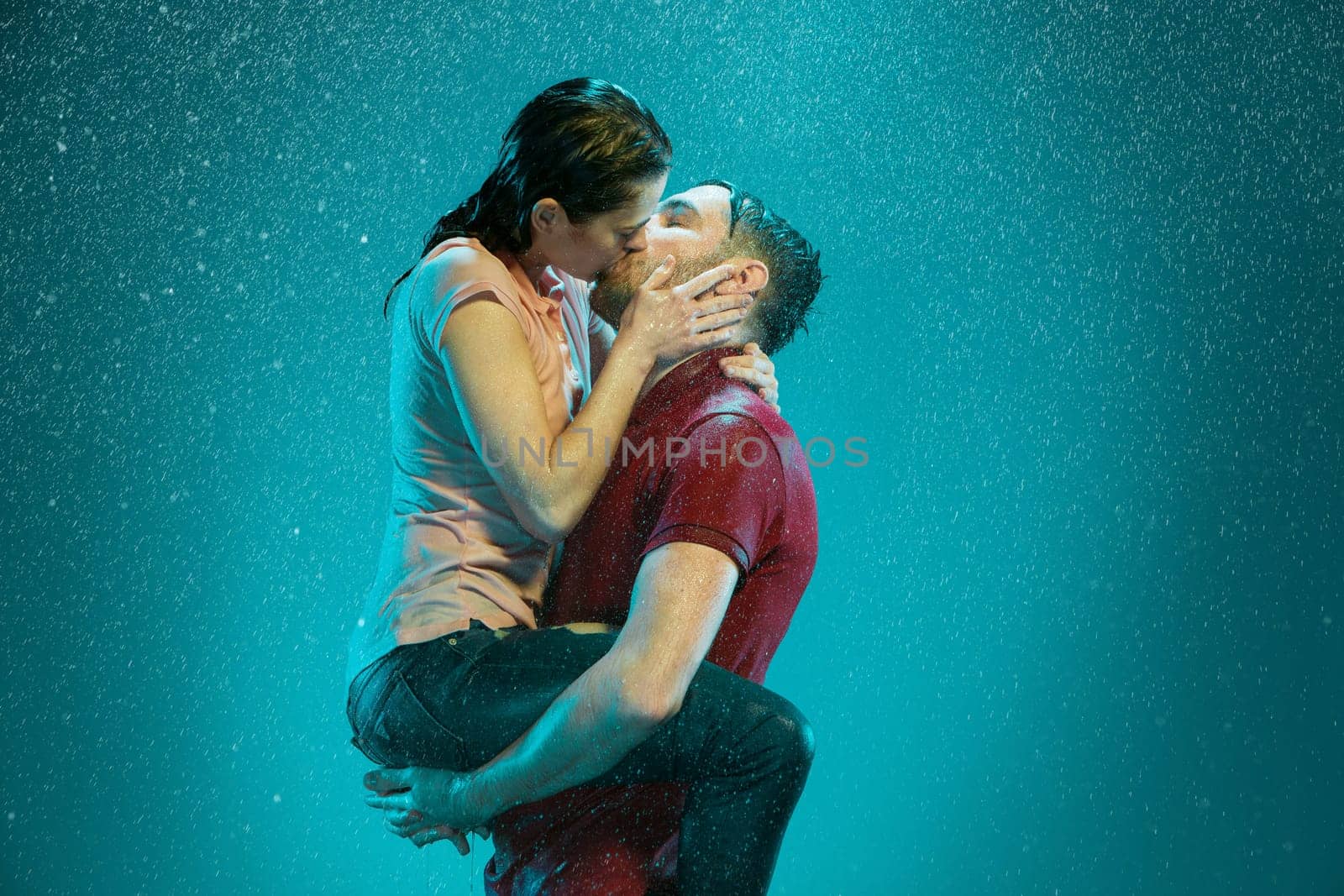 The loving couple kissing in the rain on a turquoise background