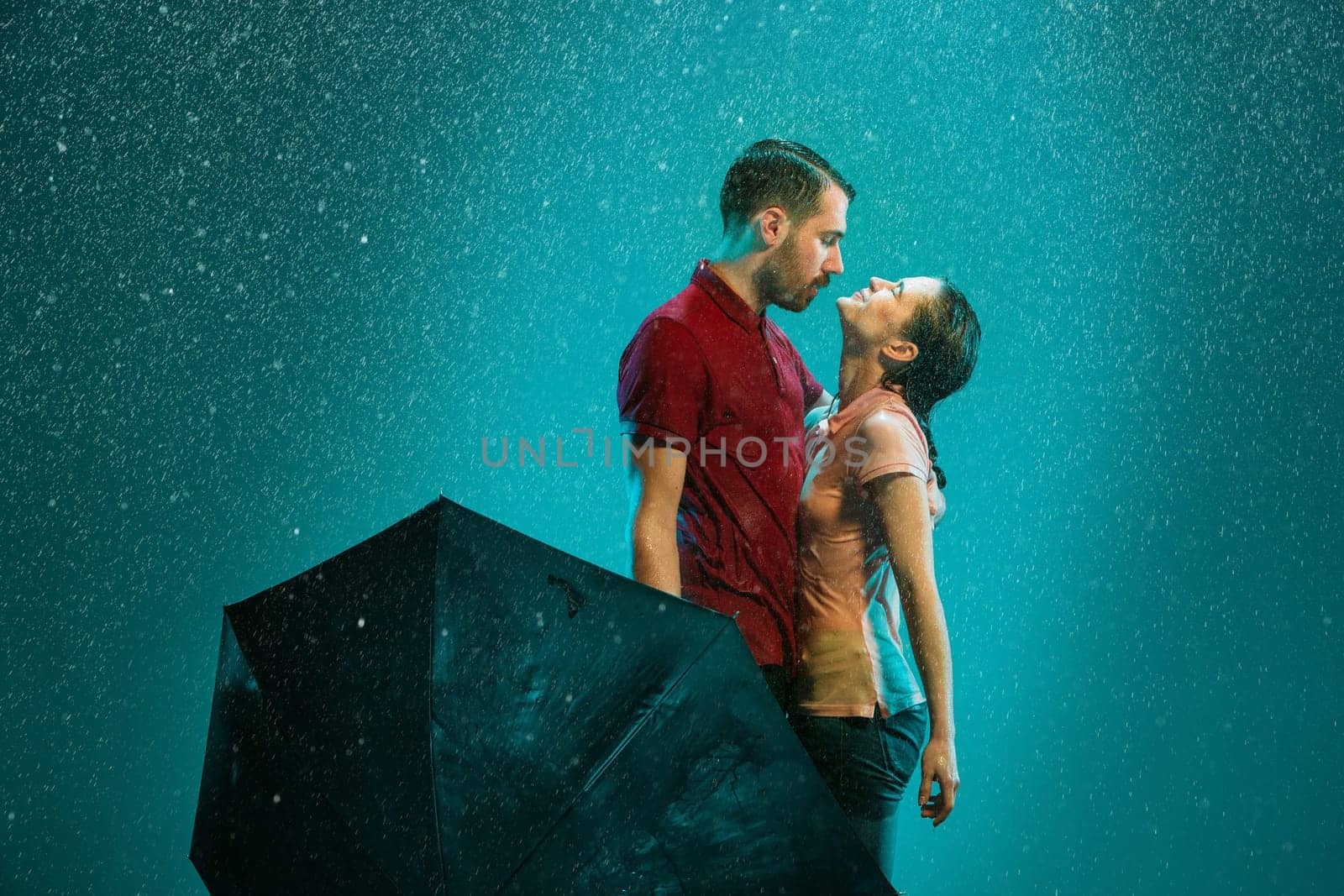 The loving couple in the rain with umbrella on a turquoise background