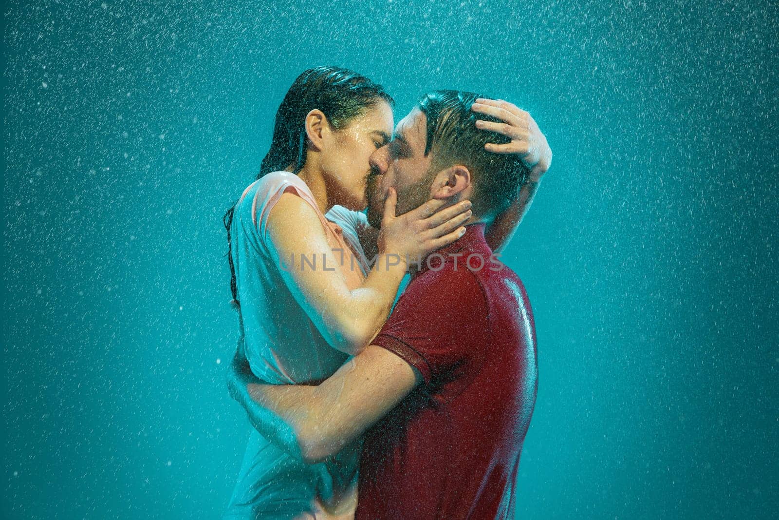 The loving couple kissing in the rain on a turquoise background