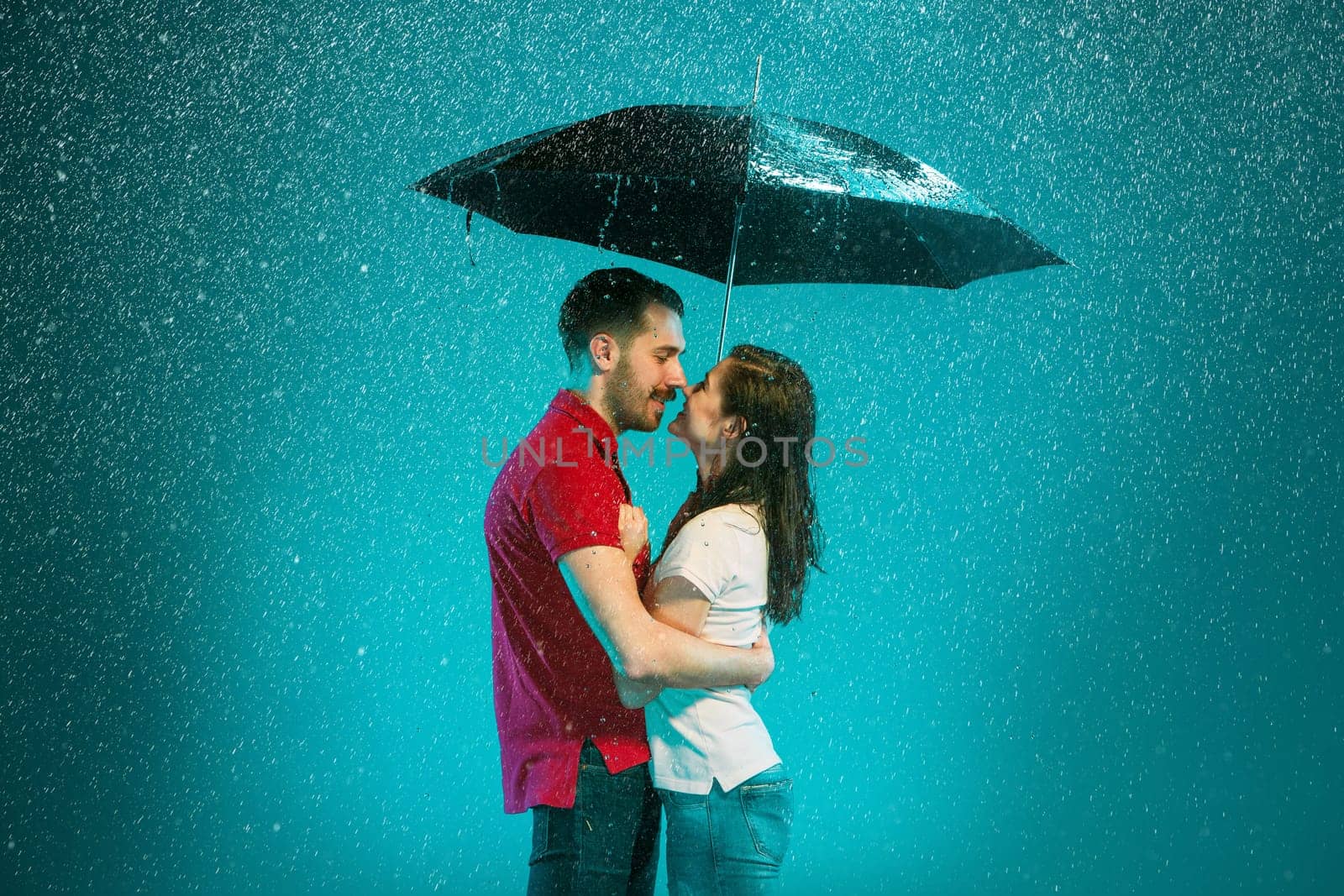 The loving couple in the rain with umbrella on a turquoise background