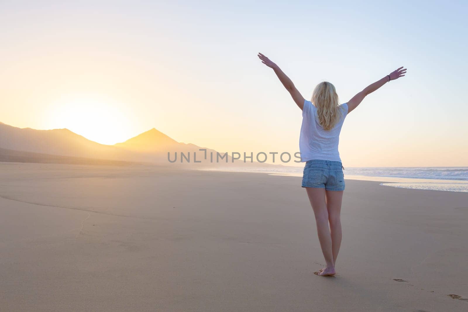 Free woman enjoying freedom feeling happy at beach at sunrise. Serene relaxing woman in pure happiness and elated enjoyment with arms raised outstretched up.