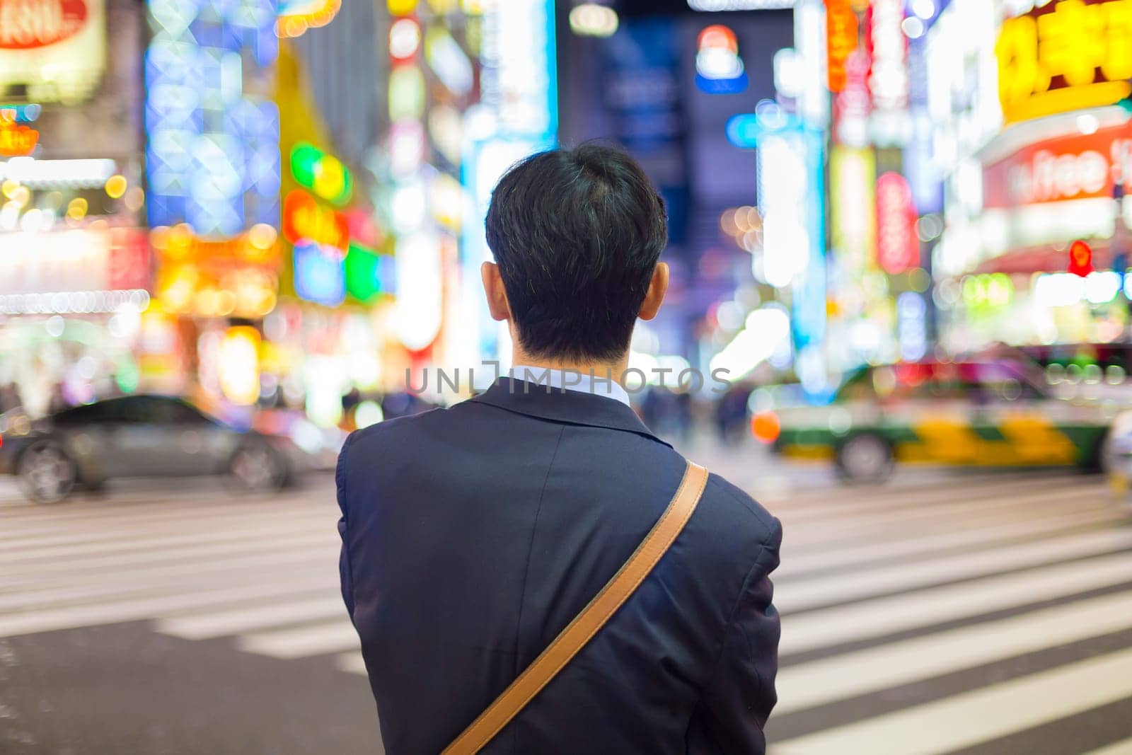 Solitary japanese corporative businessman in suit, after work, waiting on crossroad in Kabukicho, entertainment and red-light district in Shinjuku, Tokyo, Japan.