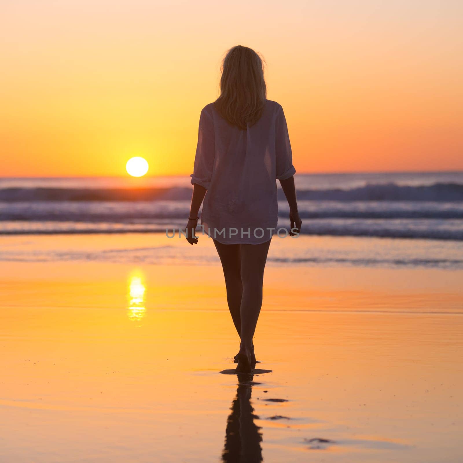 Woman walking on sandy beach in sunset leaving footprints in the sand. Beach, travel, concept. Copy space. Vertical composition.