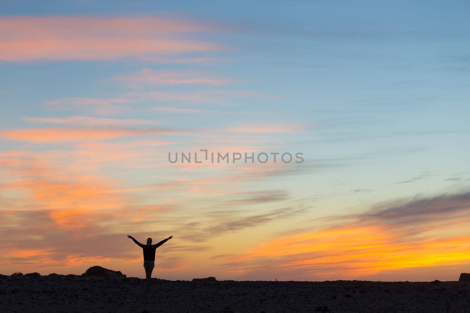Silhouette of free woman enjoying freedom feeling happy at sunset. Serene relaxing woman in pure happiness and elated enjoyment with arms raised outstretched up.