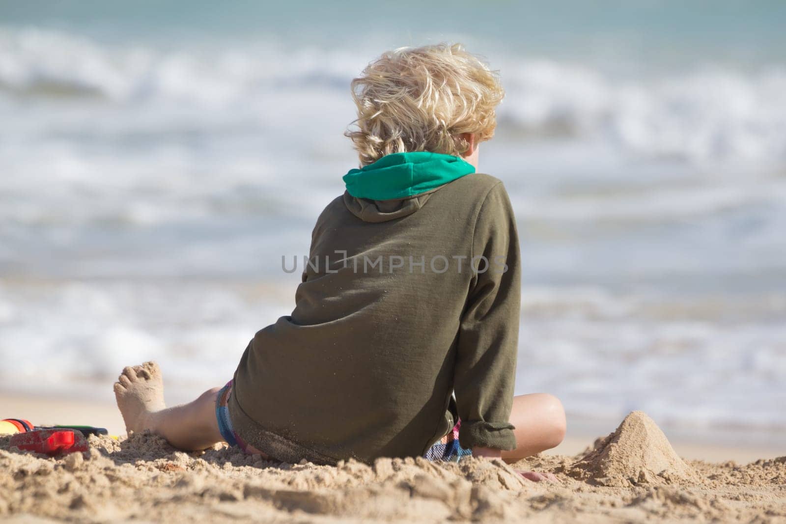 Cute child playing with beach toys on the sand. Rear view.