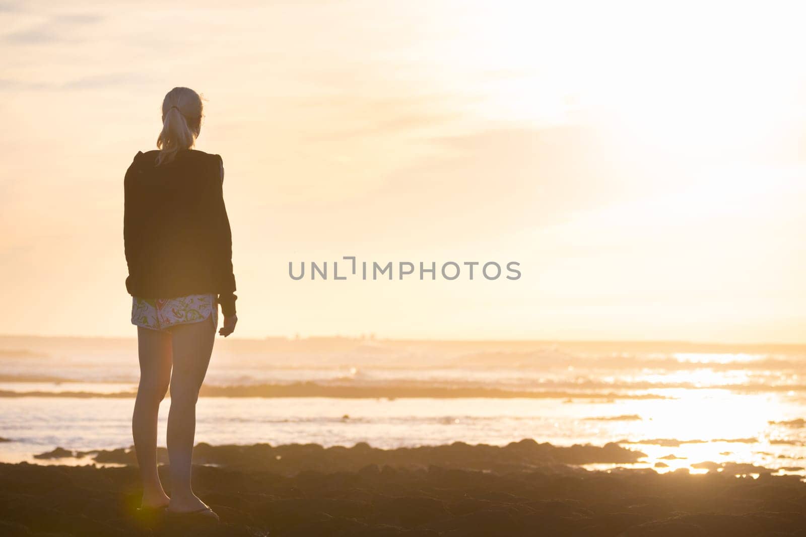 Silhouette of casualy dressed sporty woman watching sunset at the beach.