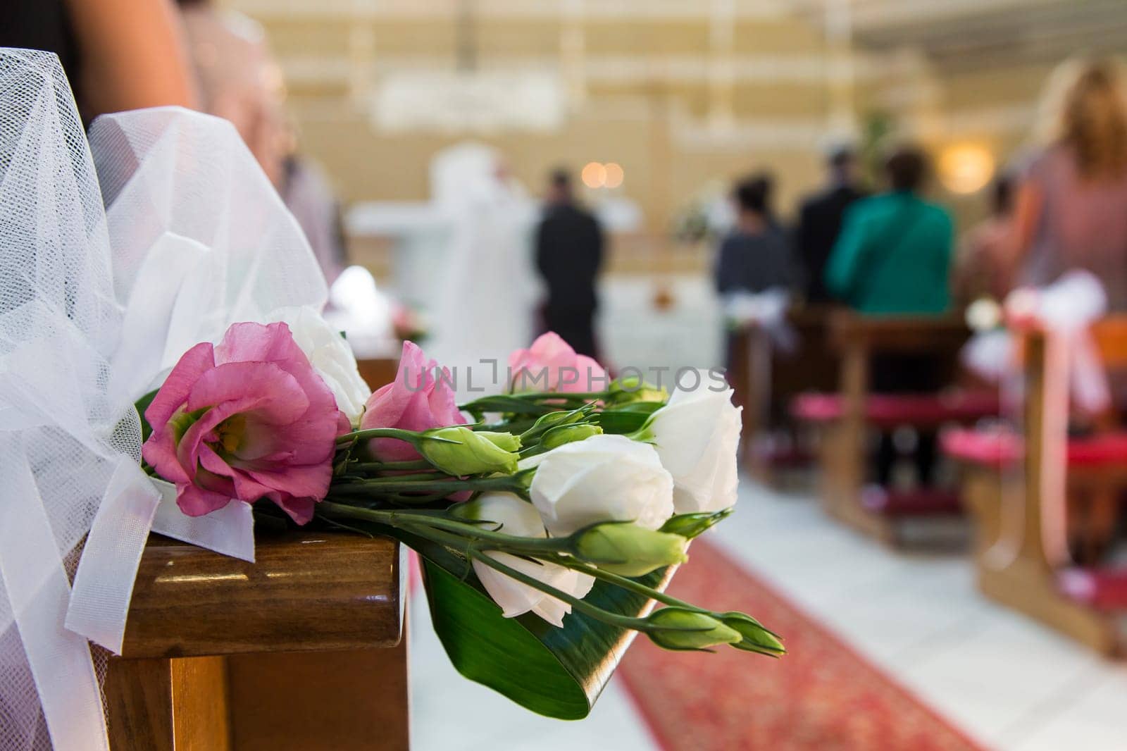 In close up view of flowers that decorate a church and the newlyweds on background