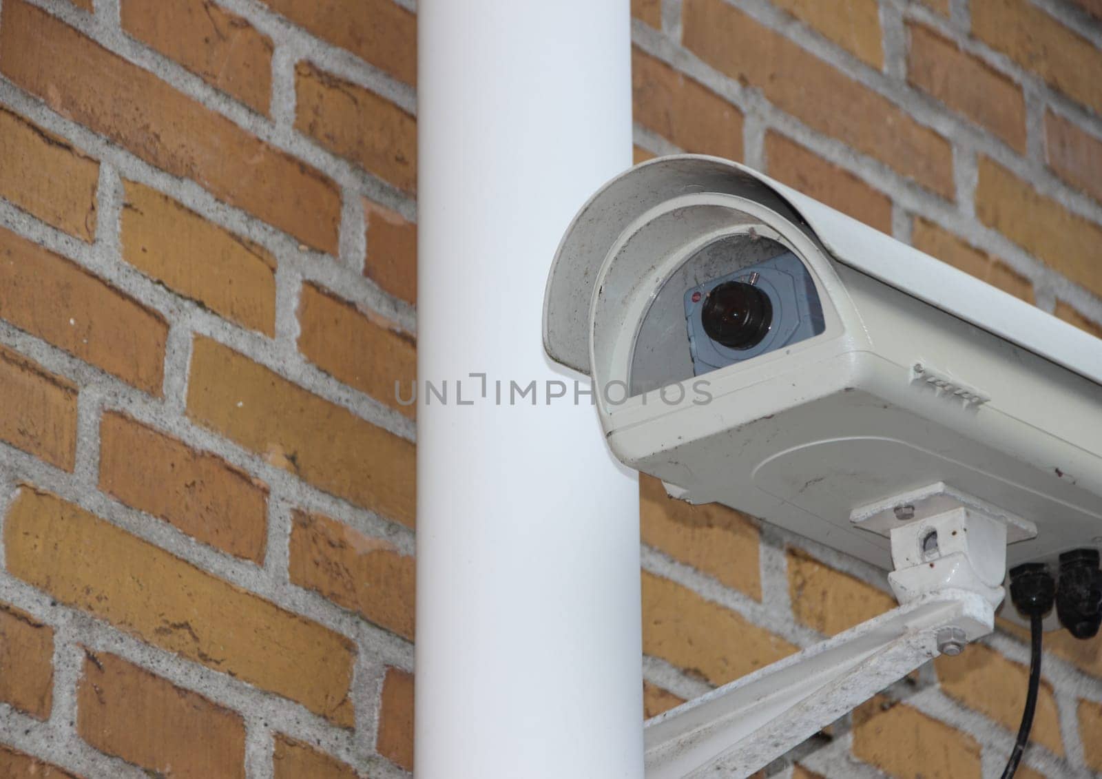 White Surveillance Camera Closeup mounted on Yellow Brick Wall