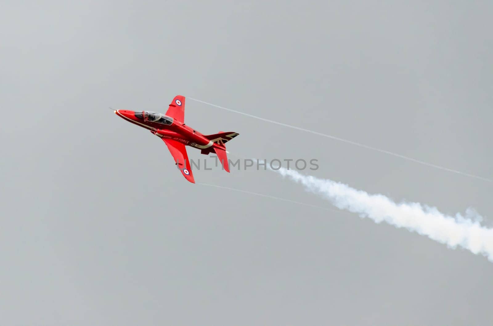 A single Red Arrow aeroplane in flight with white vapour emitting from it's tail end