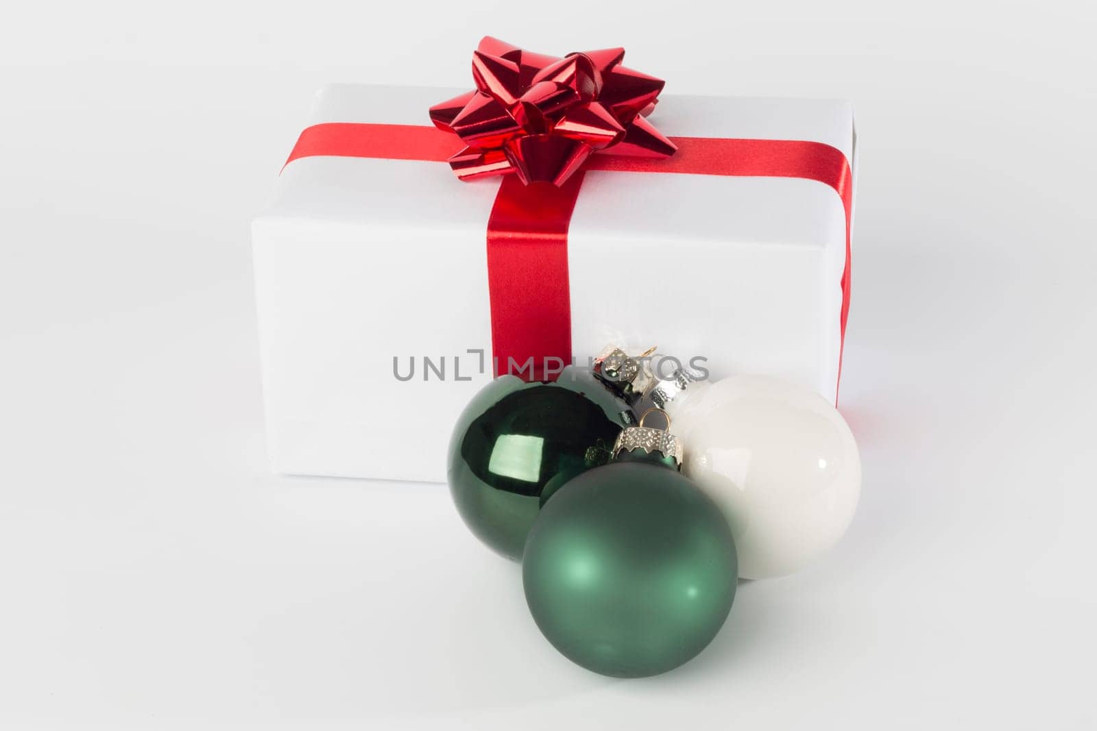 Christmas present in white paper with red ribbon and bow, green and white Christmas balls, isolated on white background