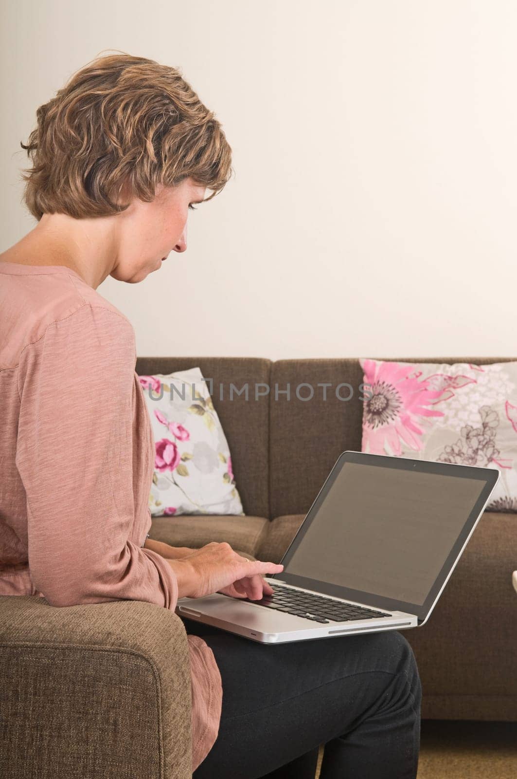 Young woman working at home on a laptop, from behind