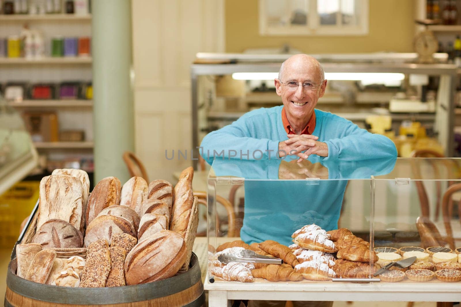 An elderly deli owner standing at the pastry display in his shop