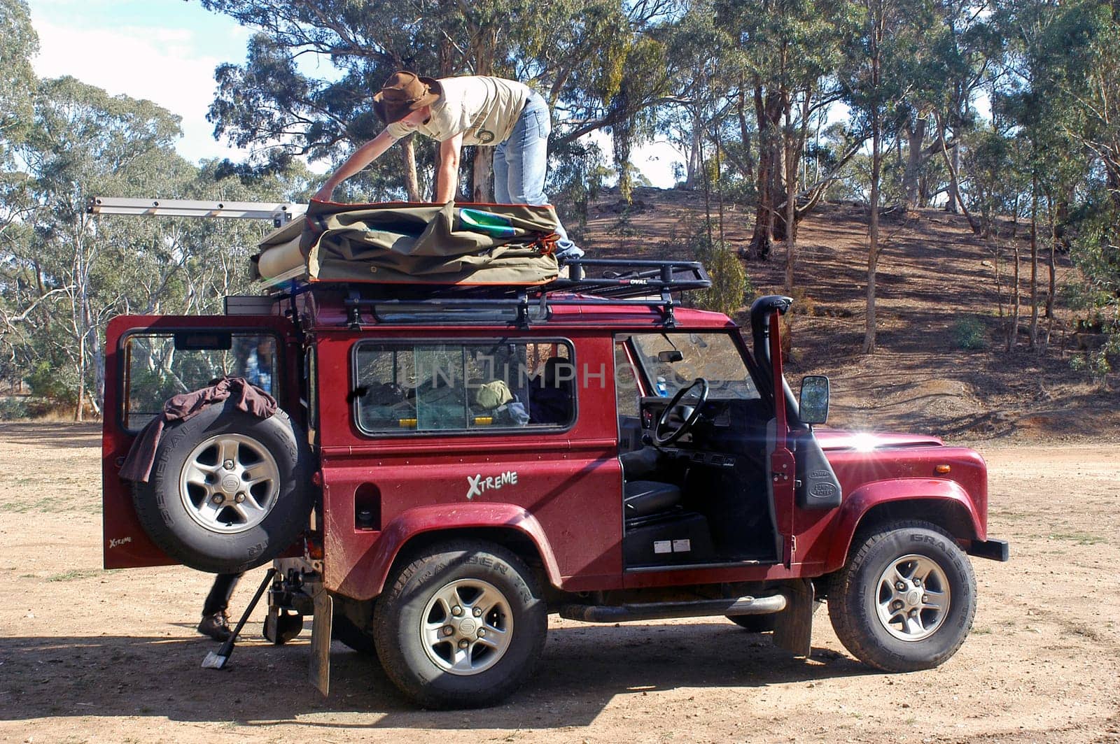 A camper fold his tent on the roof of his car in the forest where he has spent the night