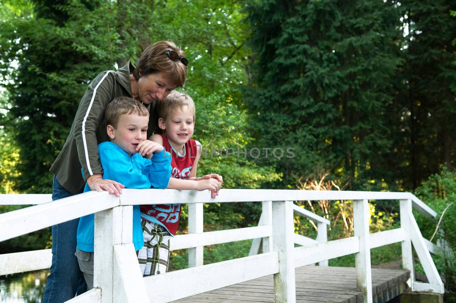 Grandma is standing on a bridge with her two grandsons, looking at a lake.