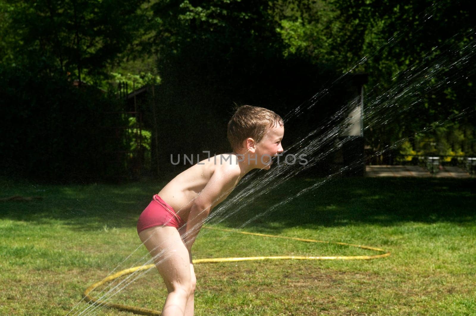 Young boy having fun playing with water from a sprinkler, during a hot day.