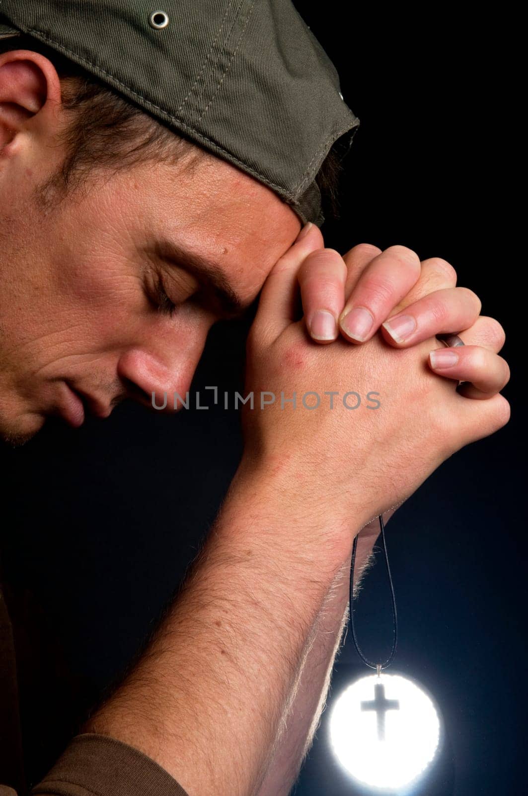 Praying man holding a cross in front of a bright light.