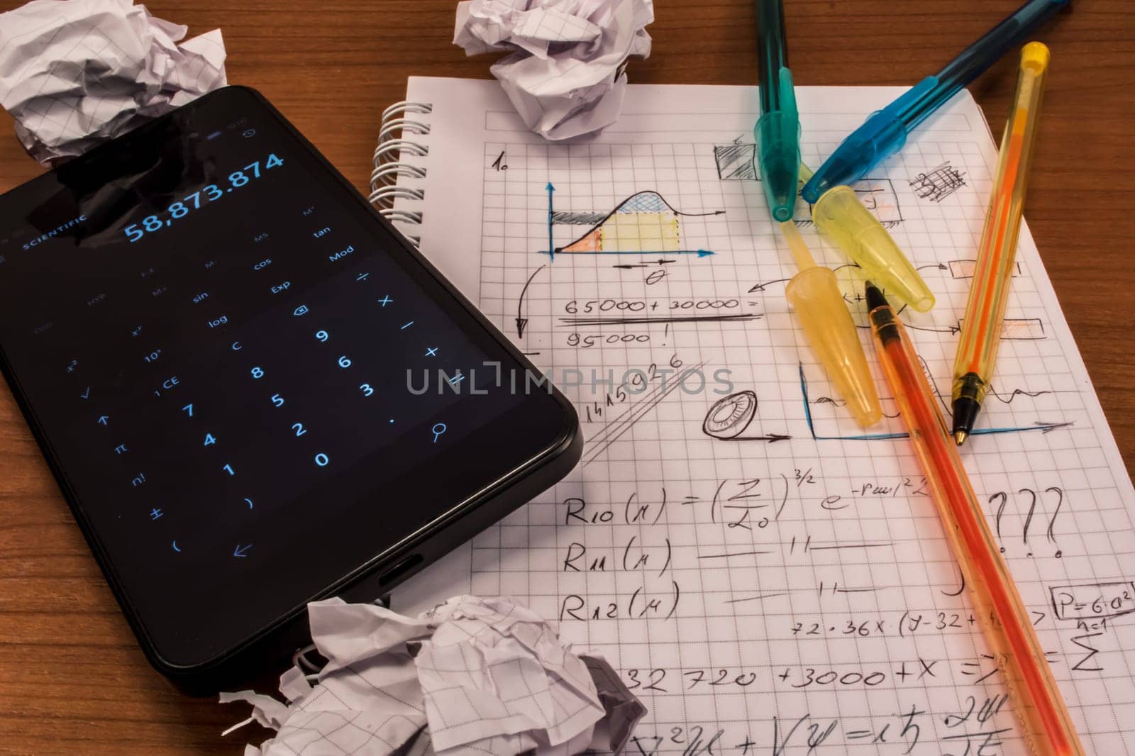 Notebook full of mathematics. Smart phone, pencils and crumpled paper are visible