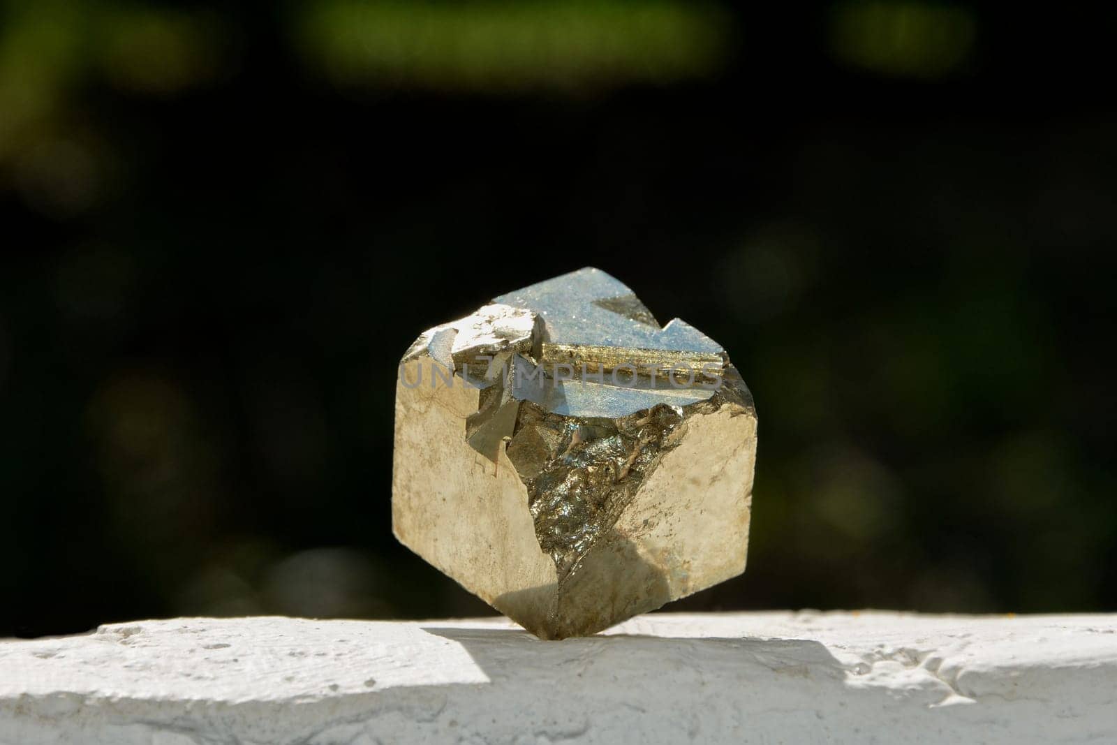 Pyrite cube stands on its corner on white wall with dark background in the sunlight