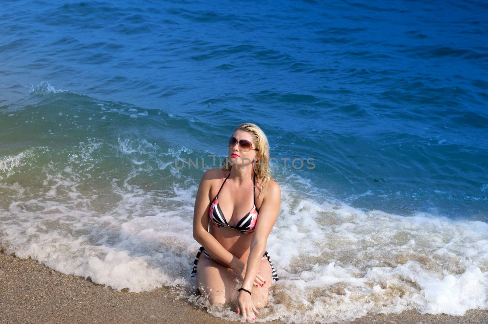 the beautiful woman sits in splashes of a surf of blue waves