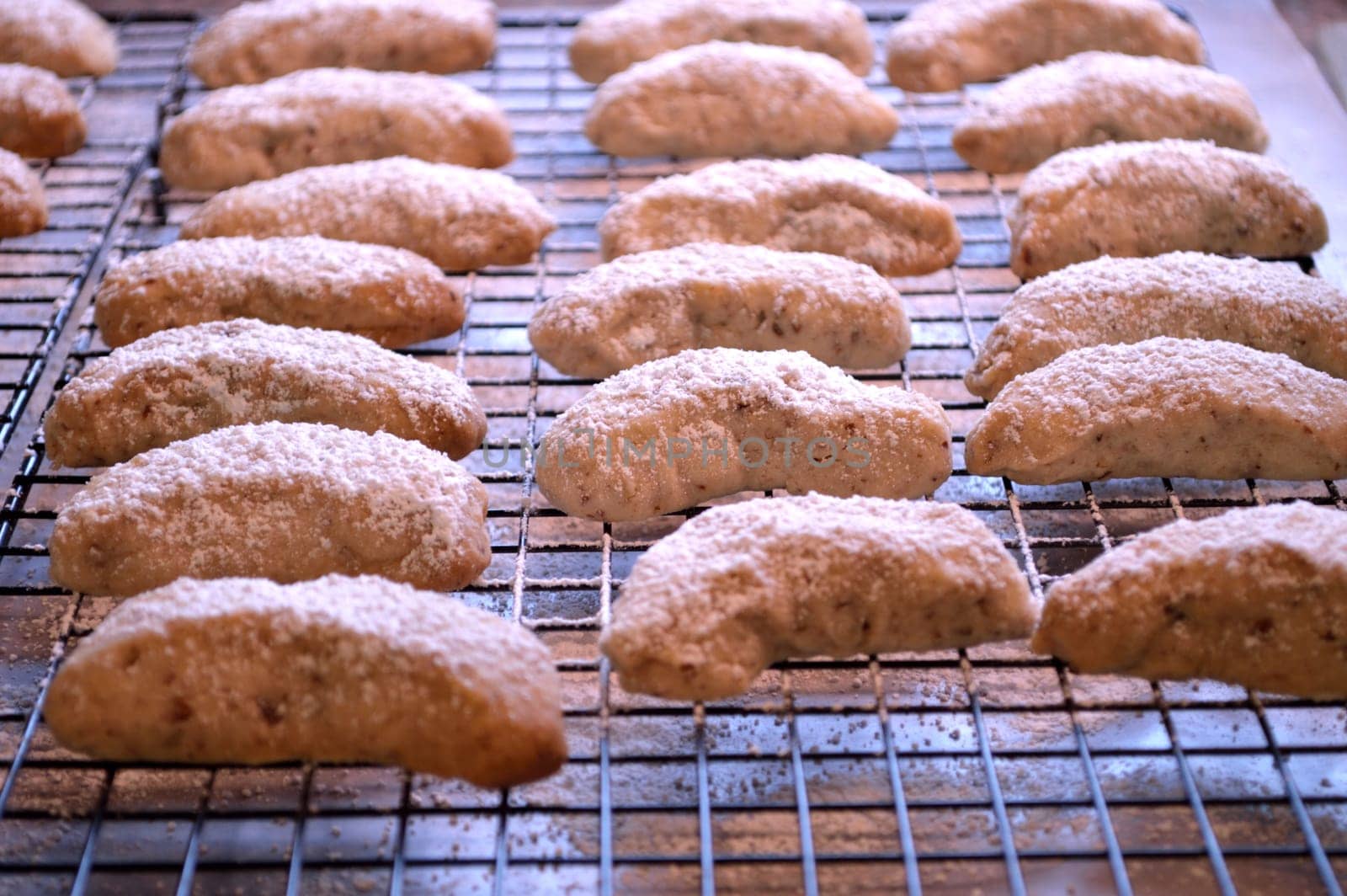 Crescent cookies, fresh out of the oven, and layed out on cooling racks to cool. Powdered sugar sprinkled on top.