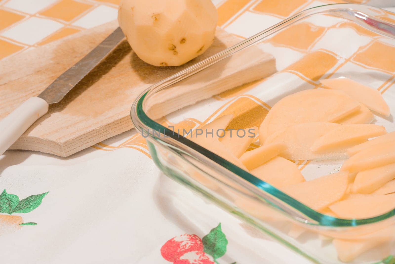 Sliced potatoes in a glass tray on a kitchen table