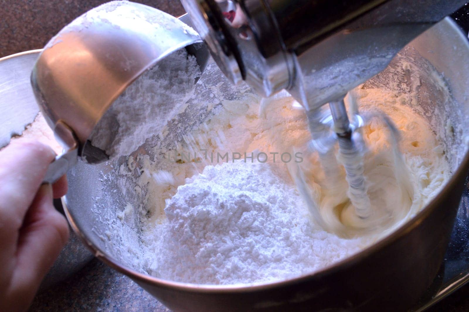 Adding 1 cup of powdered sugar to vanilla icing as its being mixed in a stainless steel stand mixer.