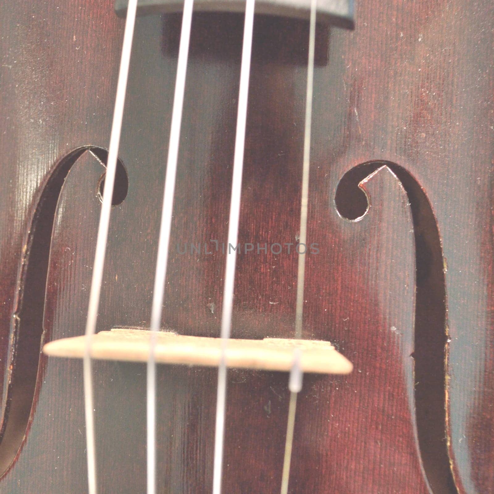 Closeup of a violin bridge and f holes, faded for text overlay.Violin is an antique from the early 1800's in a dark stain (original finish). Square composition.