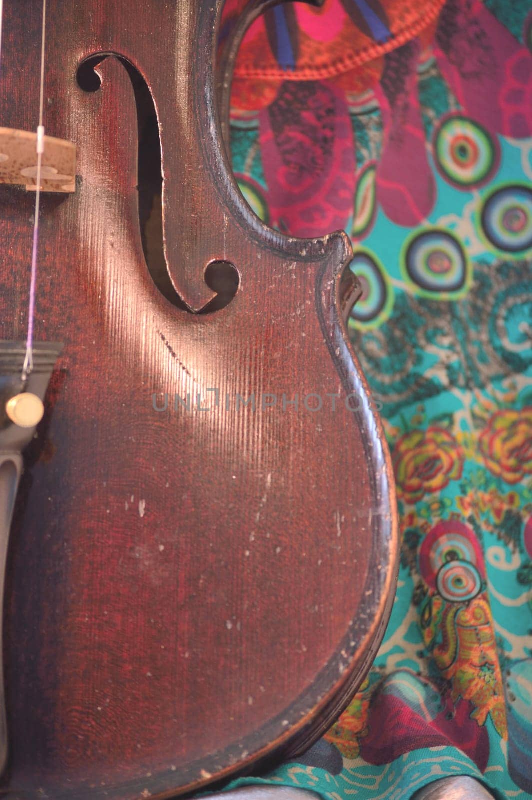 Closeup of a violin against a bright, artsy fabric background. Violin is an antique from the early 1800's in a dark stain (original finish). Vertical orientation.