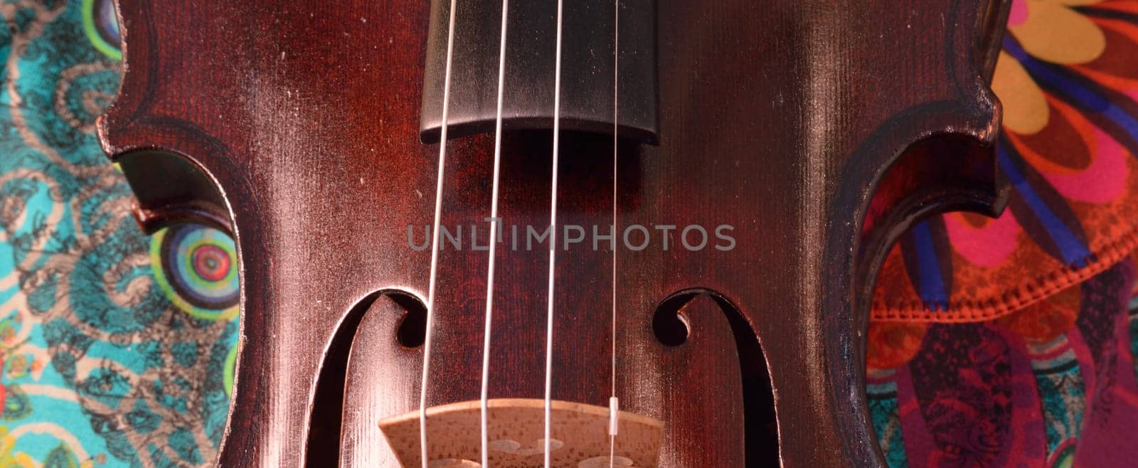 Extreme widescreen view of  the middle part of a violin.Closeup of a violin against a bright, artsy fabric background. Violin is an antique from the early 1800's in a dark stain (original finish).