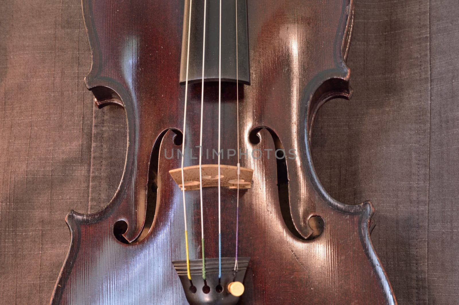 Old violin against gray seamed fabric. Violin is an antique from the early 1800's in a dark stain (original finish).