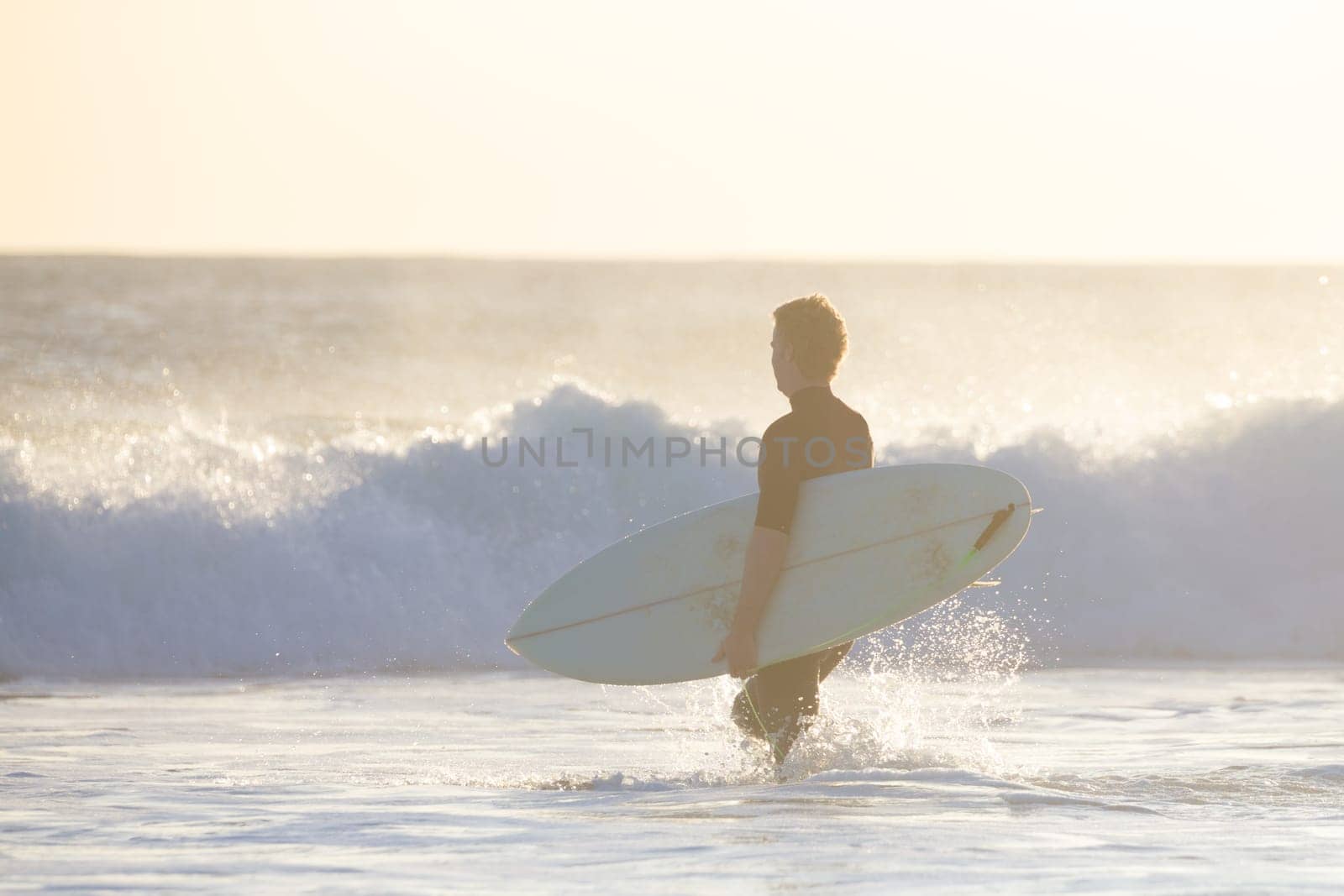 Male surfers on sandy beach with the surfboard in sunset.